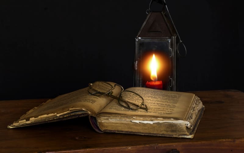 An old book, reading glasses and a lantern on a wooden table