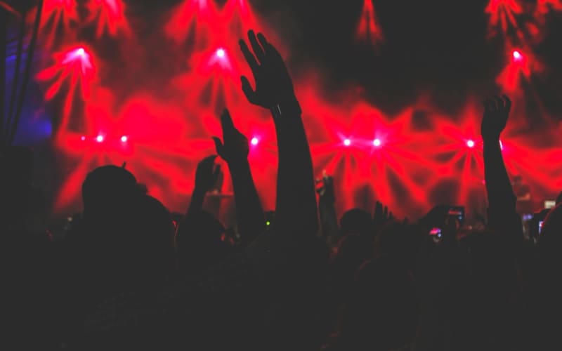 A concert crowd with hands raised under stage lights